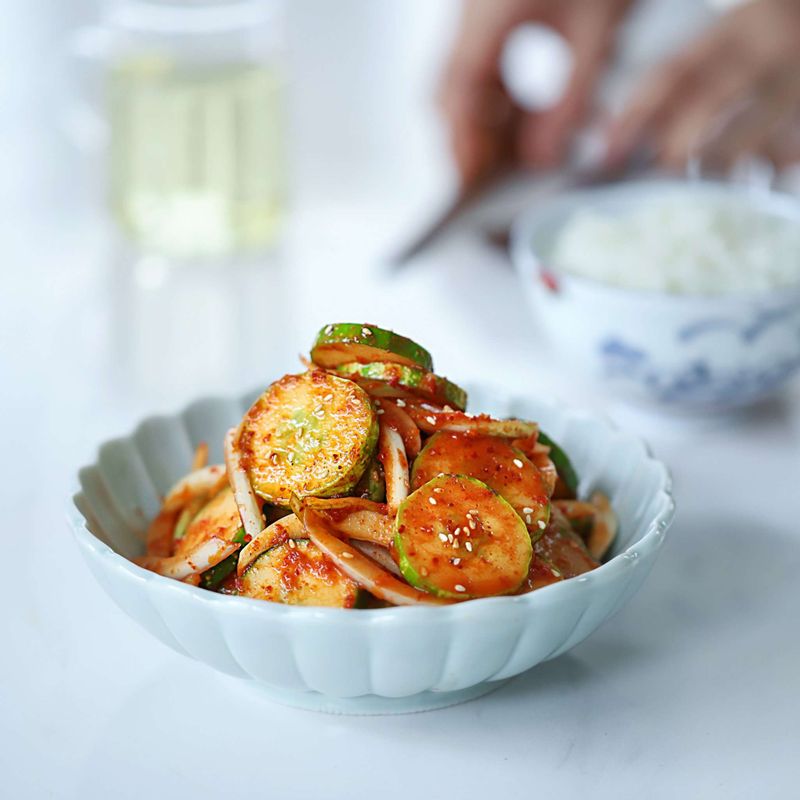 Korean cucumber salad oi muchim with sliced cucumbers, onion, garlic, and spicy gochugaru dressing in a white bowl